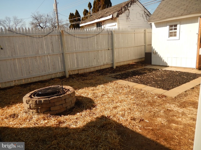 view of yard with a fire pit, a storage shed, a fenced backyard, and an outdoor structure