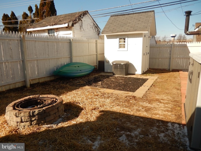 view of yard with an outbuilding, a fire pit, a fenced backyard, and a shed