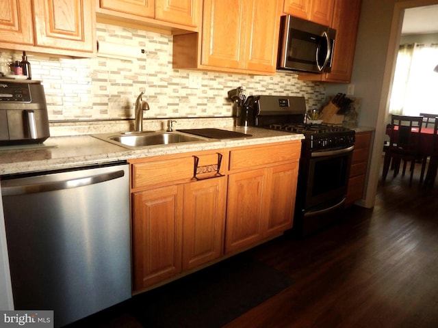 kitchen featuring a sink, backsplash, appliances with stainless steel finishes, light stone countertops, and dark wood-style flooring