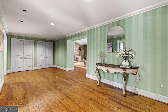 interior space with arched walkways, wood finished floors, crown molding, and baseboards