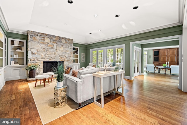 living room featuring recessed lighting, built in shelves, wood finished floors, a stone fireplace, and ornamental molding