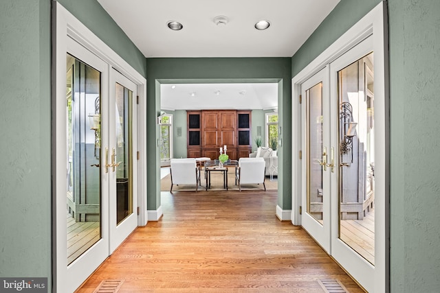 entryway with a healthy amount of sunlight, french doors, a textured wall, and light wood-style flooring
