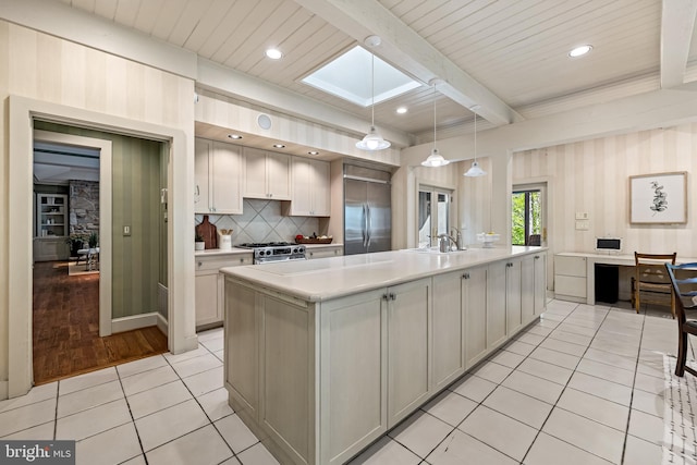 kitchen with premium appliances, a skylight, light tile patterned floors, beamed ceiling, and light countertops