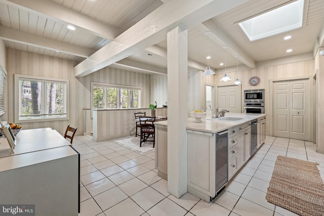 kitchen featuring a sink, beam ceiling, a skylight, light countertops, and appliances with stainless steel finishes