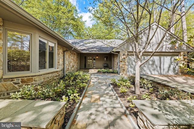 property entrance with a garage, stone siding, concrete driveway, and a shingled roof