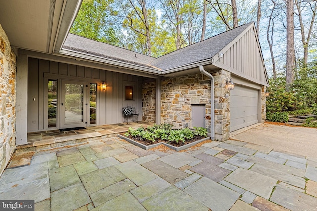 doorway to property featuring a shingled roof, board and batten siding, driveway, stone siding, and a garage