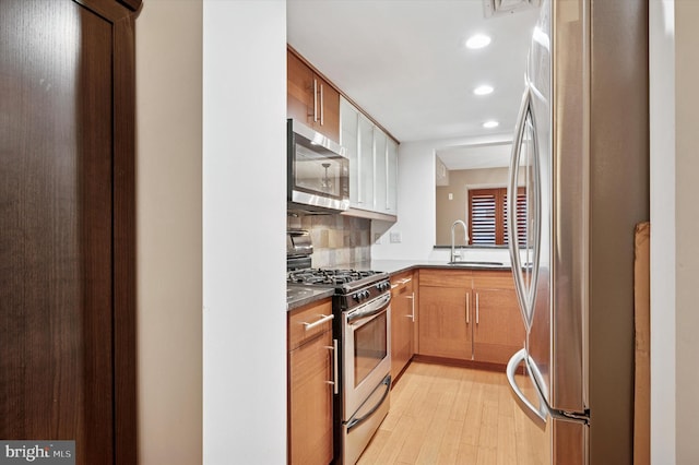 kitchen featuring light wood-style flooring, a sink, dark countertops, recessed lighting, and stainless steel appliances