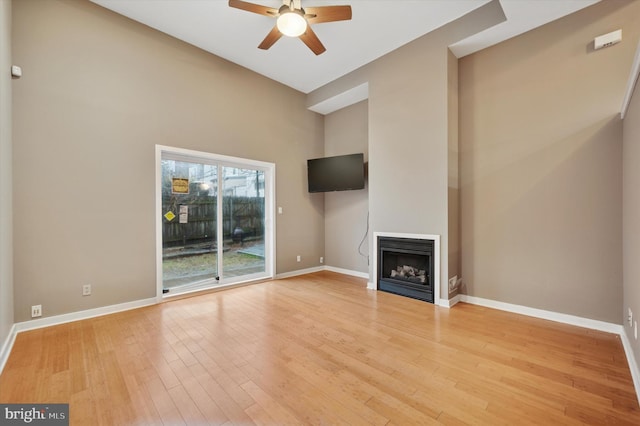 unfurnished living room with baseboards, a ceiling fan, a fireplace, and light wood finished floors