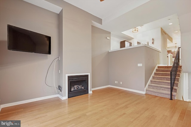 unfurnished living room with stairway, baseboards, wood finished floors, and a fireplace