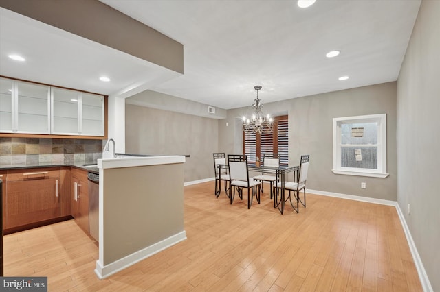 kitchen featuring light wood-type flooring, a sink, a peninsula, glass insert cabinets, and baseboards