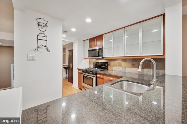 kitchen with glass insert cabinets, decorative backsplash, dark stone countertops, stainless steel appliances, and a sink