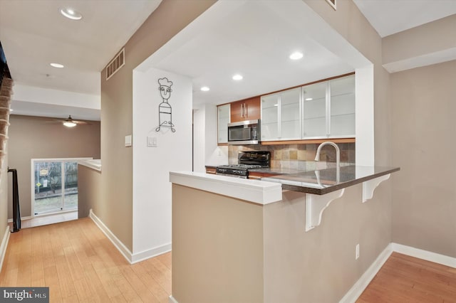 kitchen with a kitchen bar, visible vents, stainless steel microwave, backsplash, and gas range oven