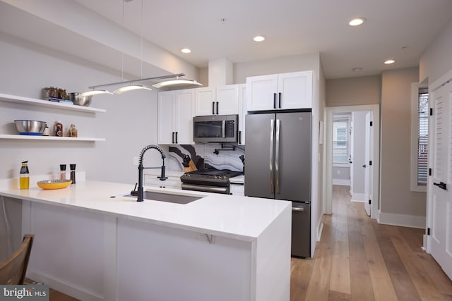 kitchen featuring light wood-style flooring, a sink, white cabinetry, stainless steel appliances, and a peninsula