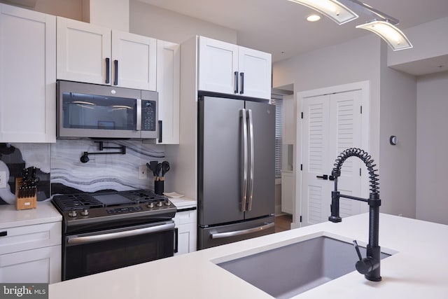 kitchen with a sink, tasteful backsplash, white cabinetry, stainless steel appliances, and light countertops