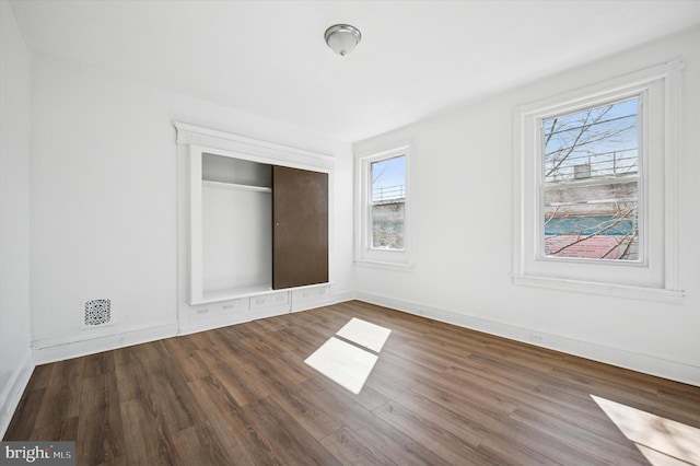 unfurnished bedroom with visible vents, wood finished floors, a closet, and baseboards