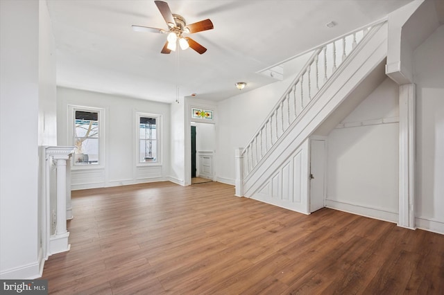 unfurnished living room with stairs, wood finished floors, and ceiling fan