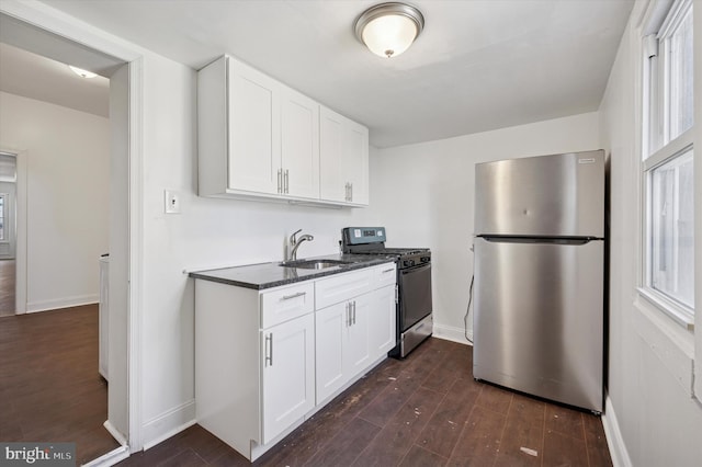 kitchen featuring dark stone countertops, appliances with stainless steel finishes, dark wood-style floors, white cabinetry, and a sink