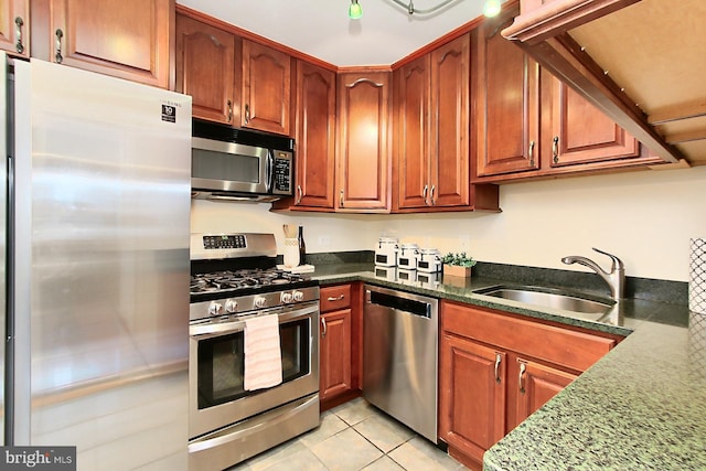 kitchen with a sink, light tile patterned floors, brown cabinetry, and stainless steel appliances