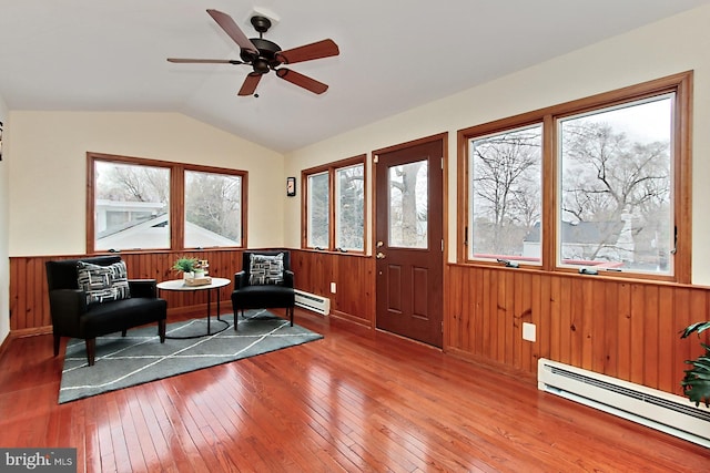 living area featuring a baseboard heating unit, lofted ceiling, hardwood / wood-style flooring, and a wainscoted wall