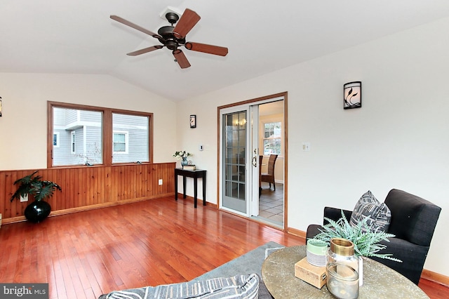 living room with wooden walls, a ceiling fan, lofted ceiling, wood-type flooring, and wainscoting