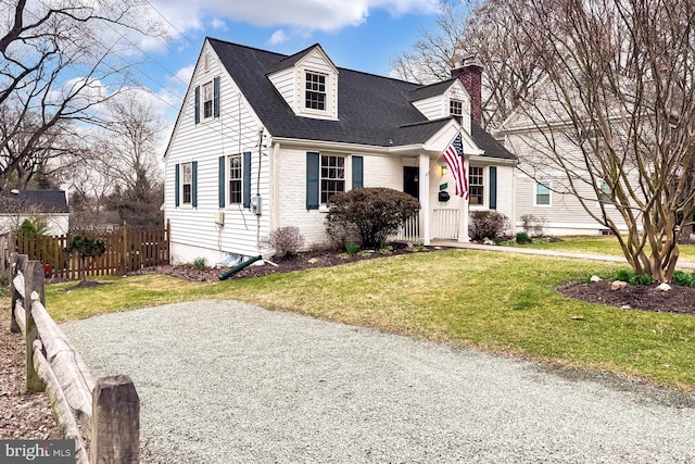 cape cod home featuring brick siding, a shingled roof, fence, a front yard, and a chimney