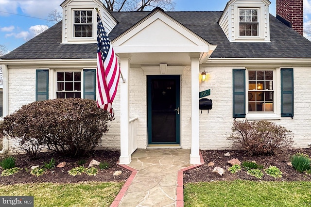 doorway to property with brick siding, roof with shingles, and a chimney