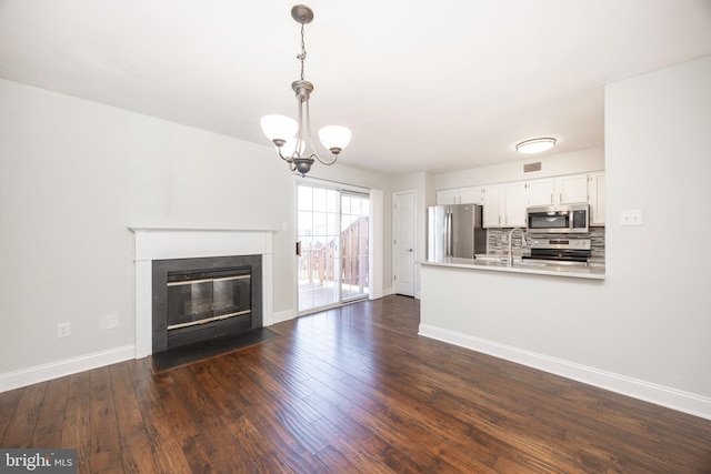 unfurnished living room featuring an inviting chandelier, a fireplace with flush hearth, dark wood-style floors, and baseboards