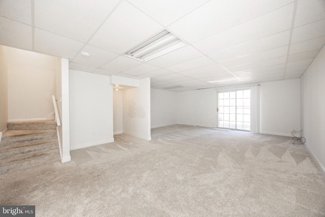 below grade area featuring carpet flooring, stairs, a paneled ceiling, and baseboards