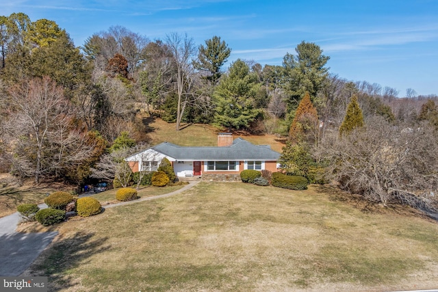 view of front of home featuring a front yard, a view of trees, and a chimney