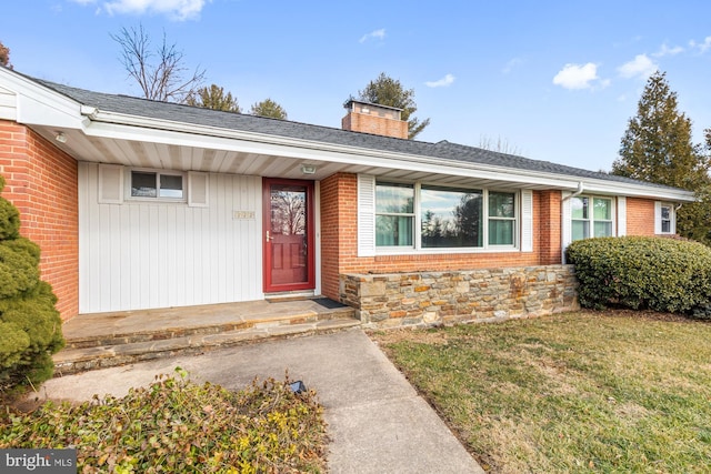 entrance to property featuring brick siding, a lawn, a chimney, and a shingled roof