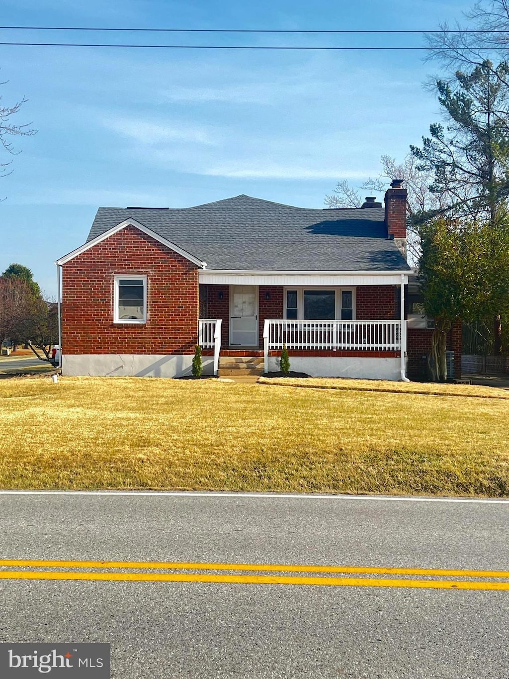 single story home featuring a porch, a front yard, a shingled roof, brick siding, and a chimney