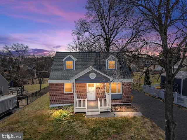 view of front of property with brick siding, a lawn, roof with shingles, and fence