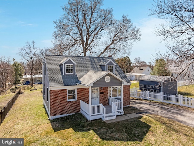 view of front of house with brick siding, roof with shingles, a front lawn, and fence