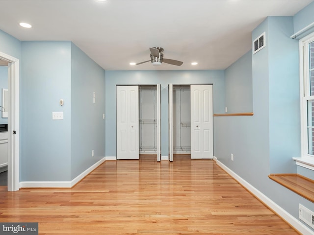 unfurnished bedroom featuring visible vents, multiple closets, light wood-style floors, and baseboards