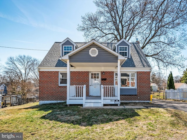 new england style home with brick siding, roof with shingles, a front lawn, and fence