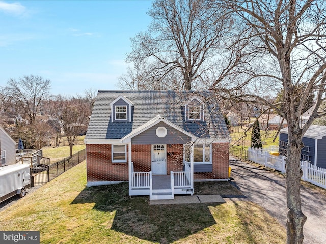 view of front facade featuring brick siding, a shingled roof, a front yard, and fence