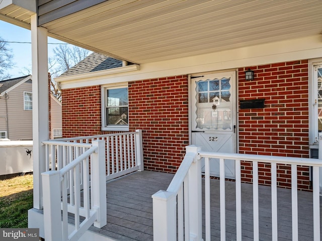 doorway to property with brick siding and roof with shingles