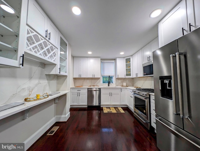 kitchen featuring a sink, backsplash, white cabinets, glass insert cabinets, and high end appliances