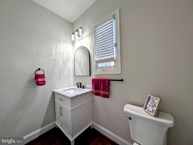 half bathroom featuring vanity, toilet, and baseboards