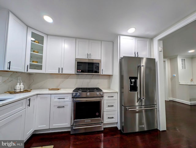 kitchen featuring light stone counters, backsplash, stainless steel appliances, white cabinets, and glass insert cabinets