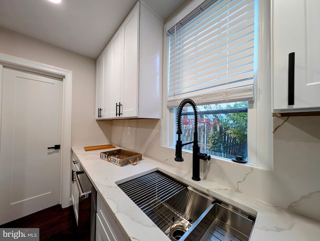 kitchen with a sink, light stone counters, dishwashing machine, white cabinetry, and dark wood-style flooring