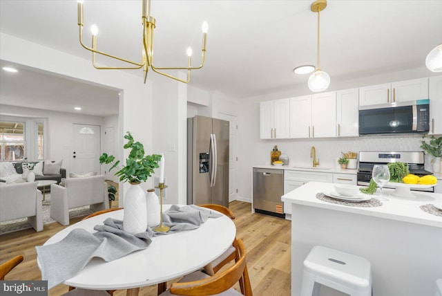 kitchen with a sink, stainless steel appliances, light countertops, white cabinets, and light wood-style floors