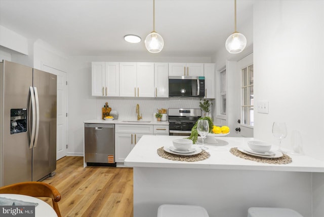 kitchen with pendant lighting, light countertops, appliances with stainless steel finishes, a peninsula, and a sink