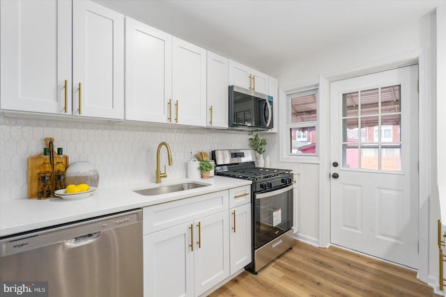 kitchen with white cabinets, appliances with stainless steel finishes, light wood-type flooring, and a sink