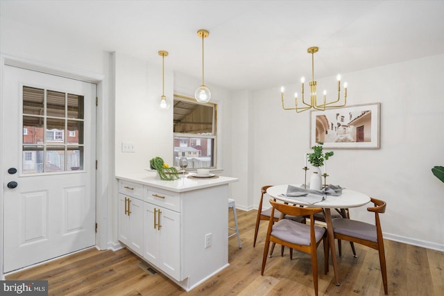 kitchen with a notable chandelier, light wood-style floors, a peninsula, white cabinets, and light countertops