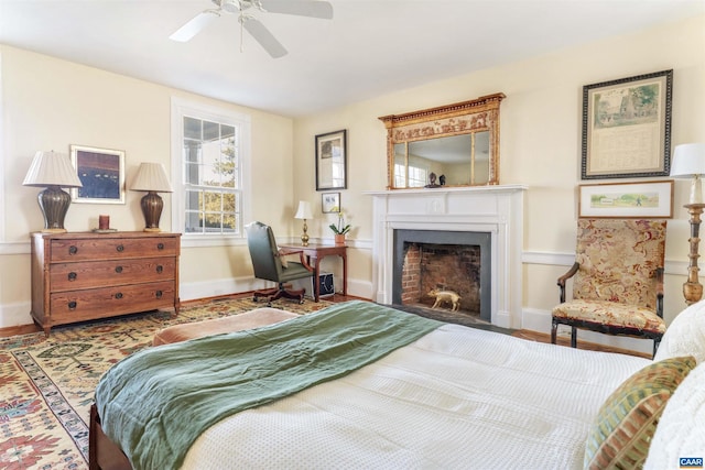 bedroom with a fireplace with flush hearth, baseboards, a ceiling fan, and wood finished floors