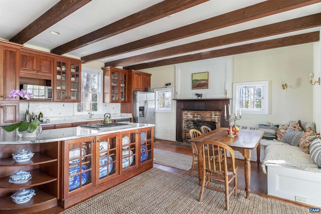 kitchen featuring glass insert cabinets, appliances with stainless steel finishes, beamed ceiling, wood finished floors, and light stone countertops