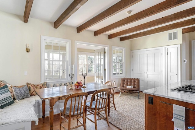 dining room featuring visible vents, beam ceiling, and light wood-style floors