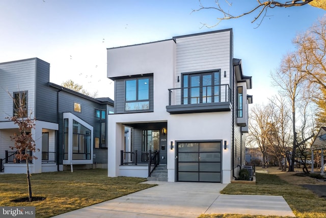 contemporary home featuring a garage, stucco siding, a front lawn, and a balcony