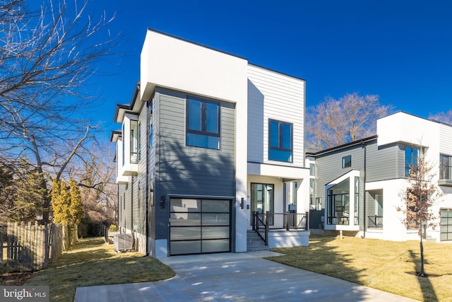 modern home featuring a front lawn, fence, cooling unit, concrete driveway, and a garage